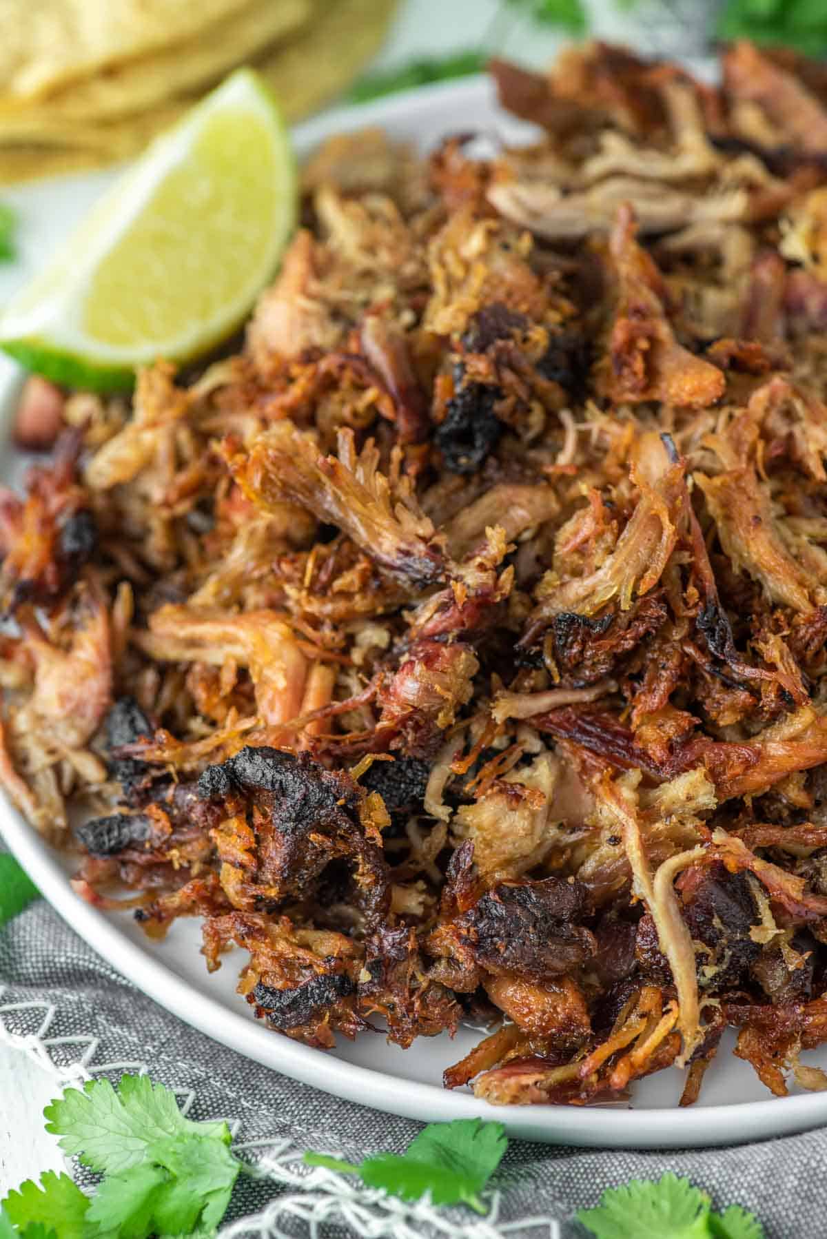 close-up shot of smoked carnitas on white plate with lime wedge