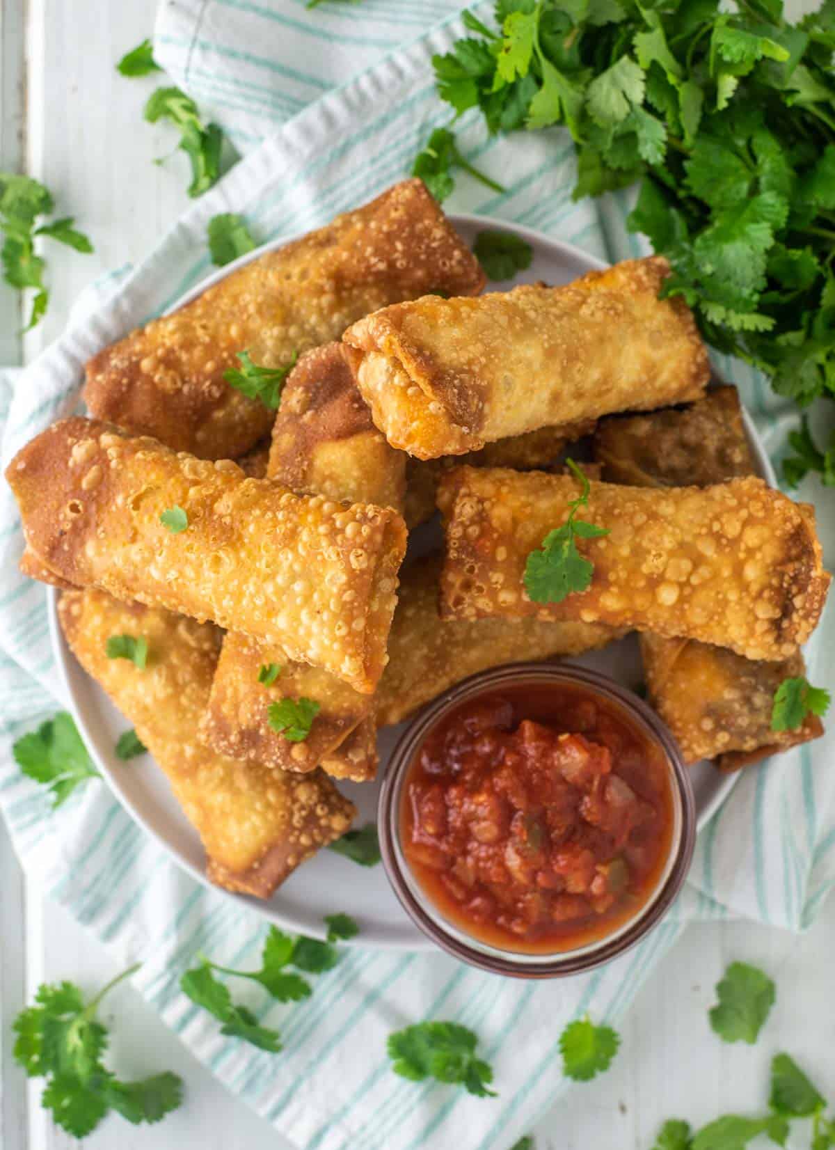 overhead shot of taco egg rolls stacked on top of each other with bowl of salsa