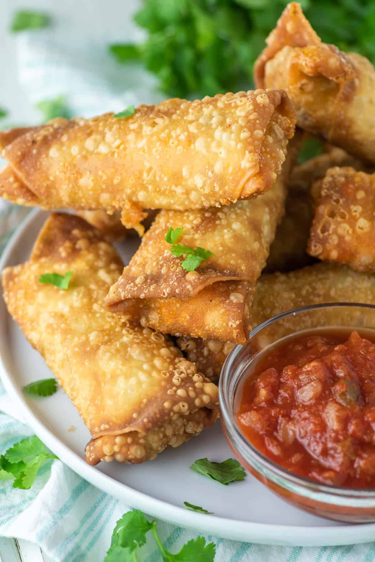 taco egg rolls stacked on top of each other with bowl of salsa