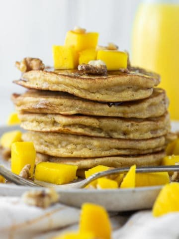 stacked pancakes with mangos on top on plate