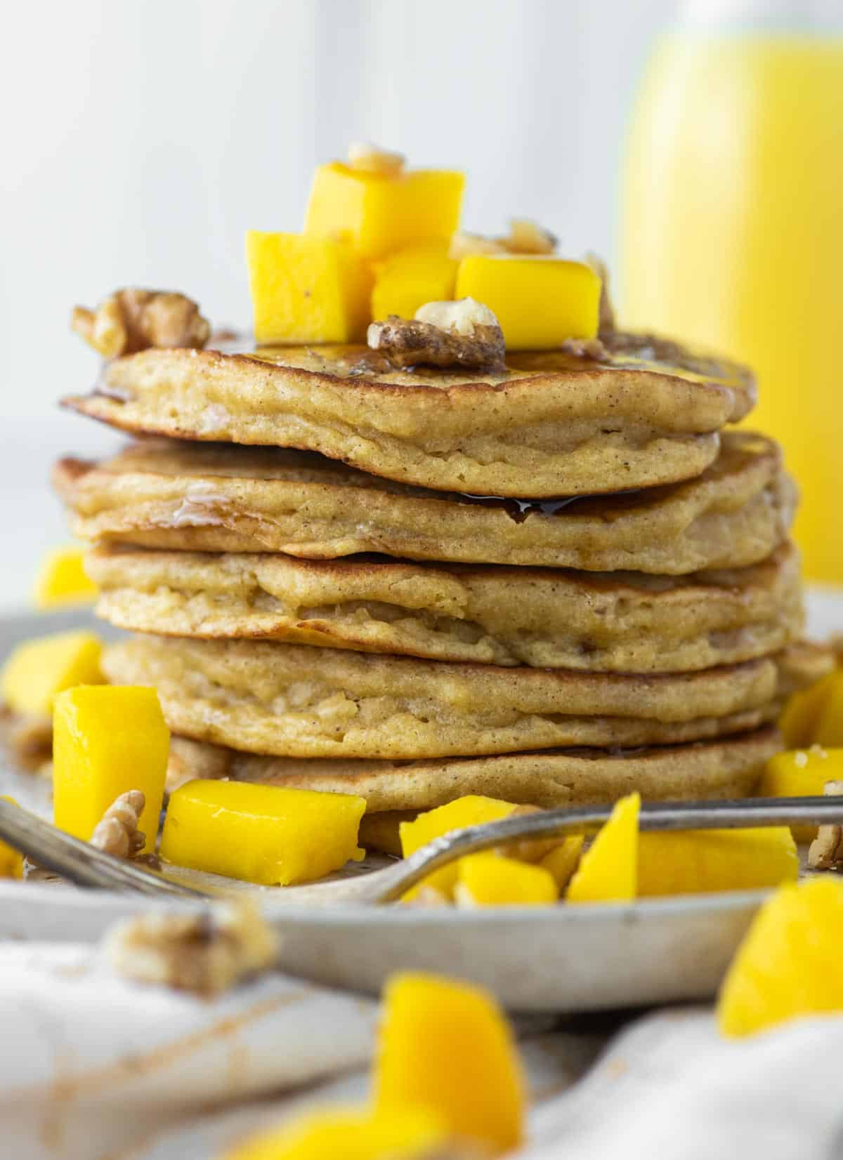 stacked pancakes with mangos on top on plate