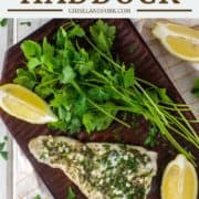 overhead shot of grilled haddock on wood board with lemon and herbs