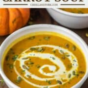 white bowl of pumpkin carrot soup with cream drizzled over it