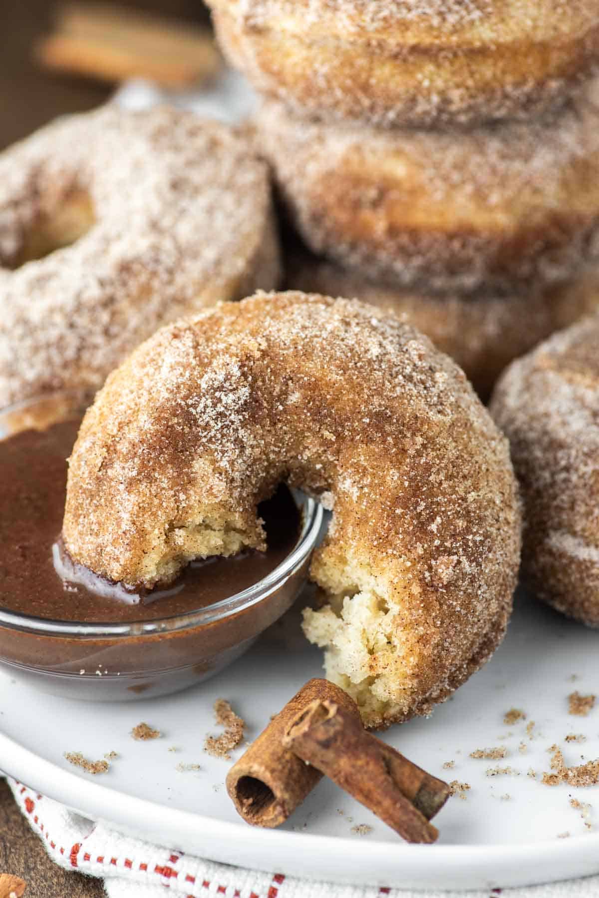 churro donut with bite taken out dipped in bowl of chocolate sauce