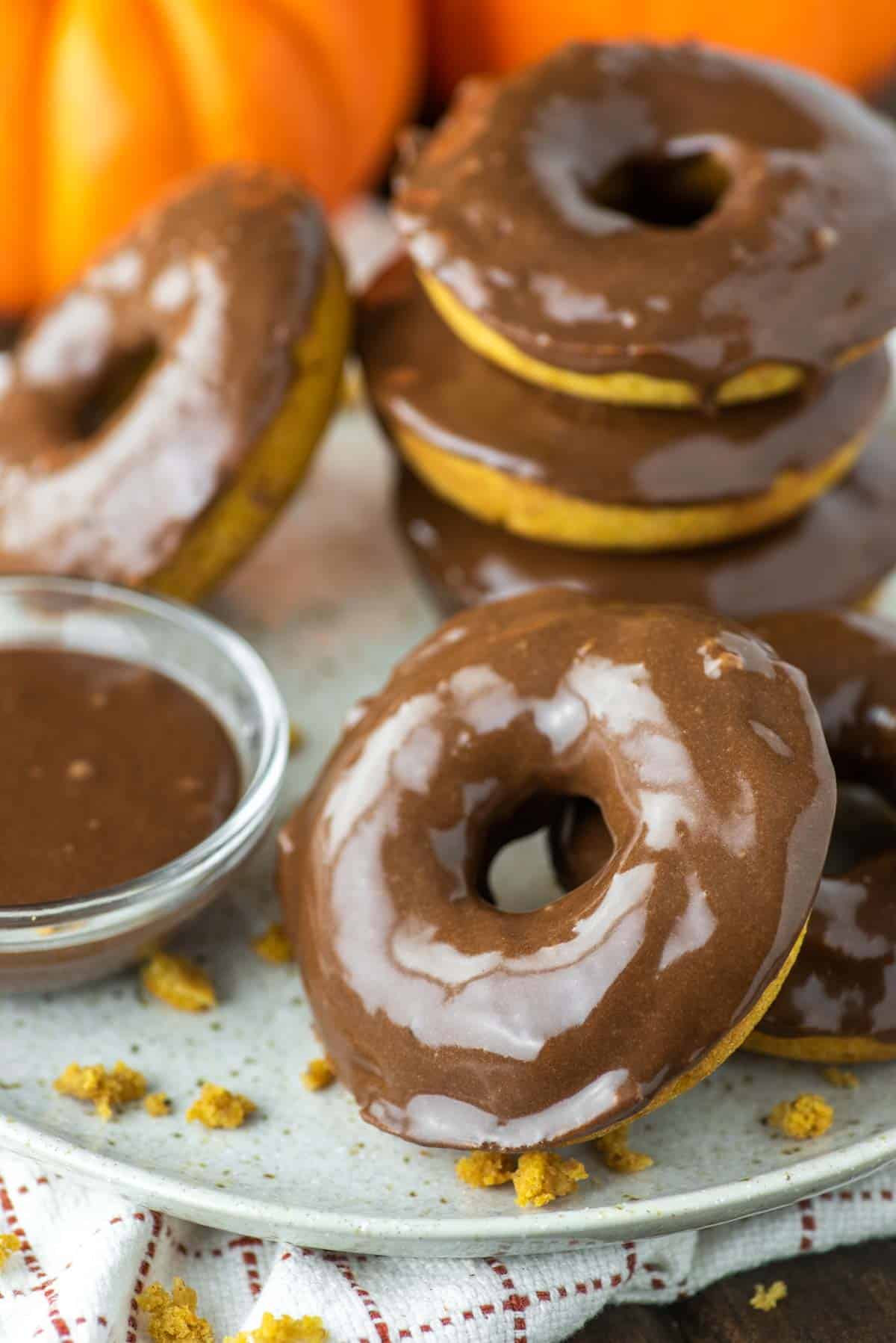 baked pumpkin donuts with chocolate glaze on plate with pumpkins in the background