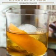 chocolate old fashioned in glass with large ice ball with bitters and whiskey in background