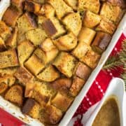 overhead shot of eggnog bread pudding in red baking pan with bowl of rum sauce