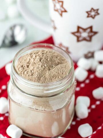 homemade hot chocolate mix in glass jar with mug behind it