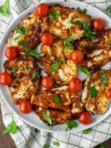 overhead shot of halloumi that is fried on white plate with tomatoes, basil and balsamic vinegar