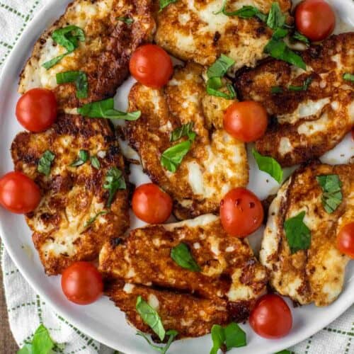 overhead shot of halloumi that is fried on white plate with tomatoes, basil and balsamic vinegar