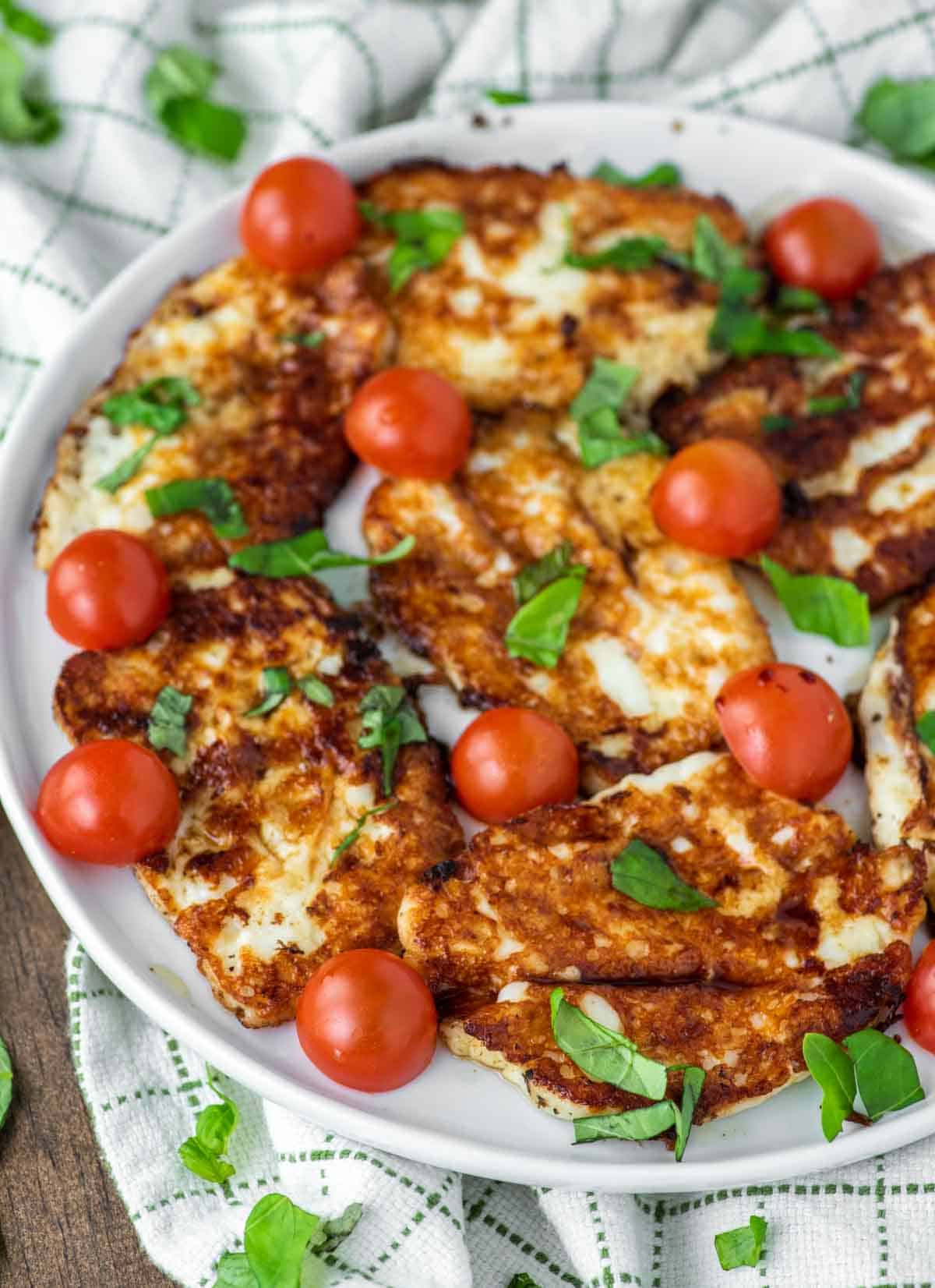 close-up of fried halloumi on white plate with tomatoes, basil and balsamic vinegar