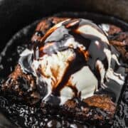 brownie in skillet topped with ice cream and sizzled chocolate sauce