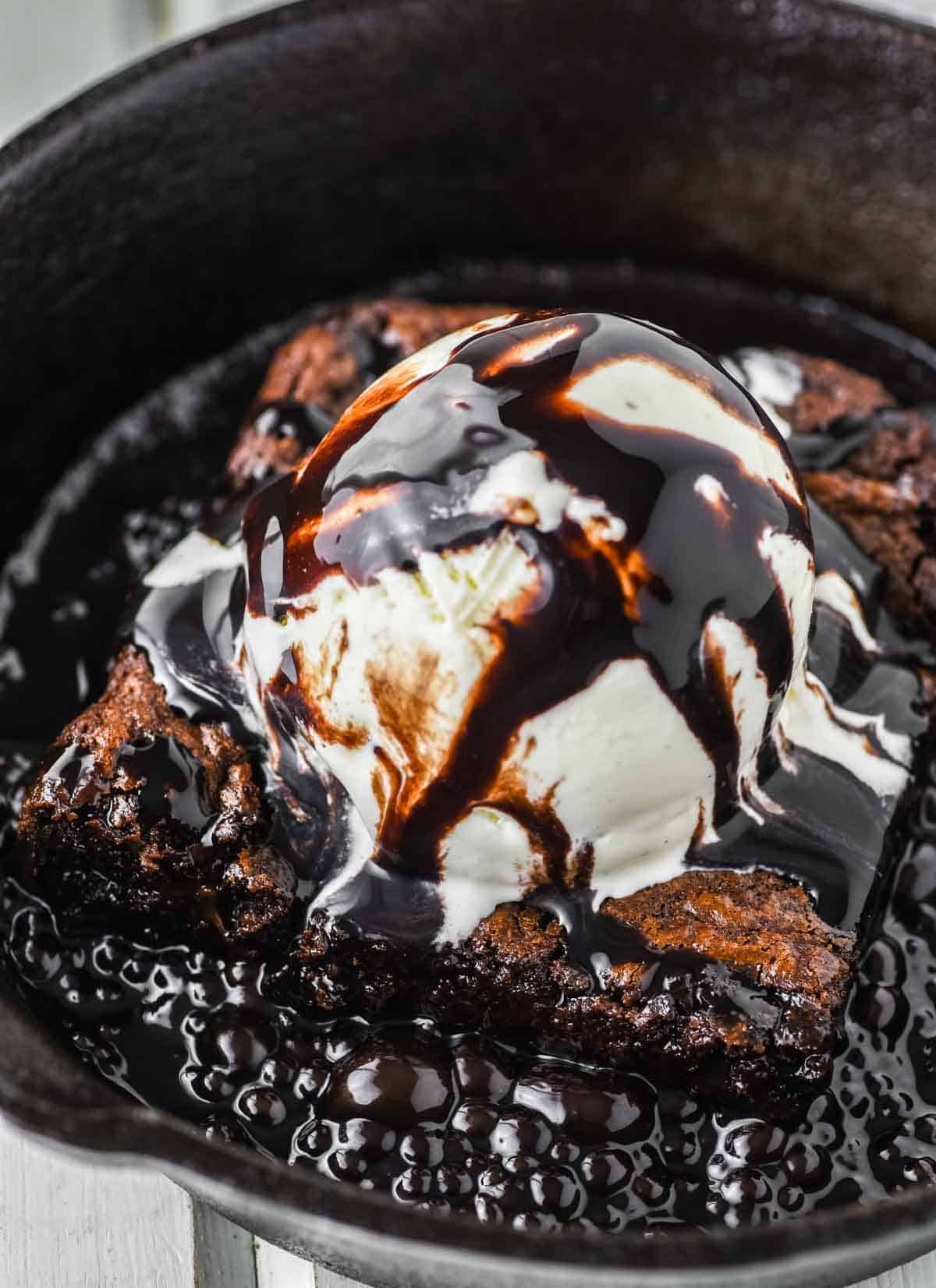 brownie in skillet topped with ice cream and sizzled chocolate sauce