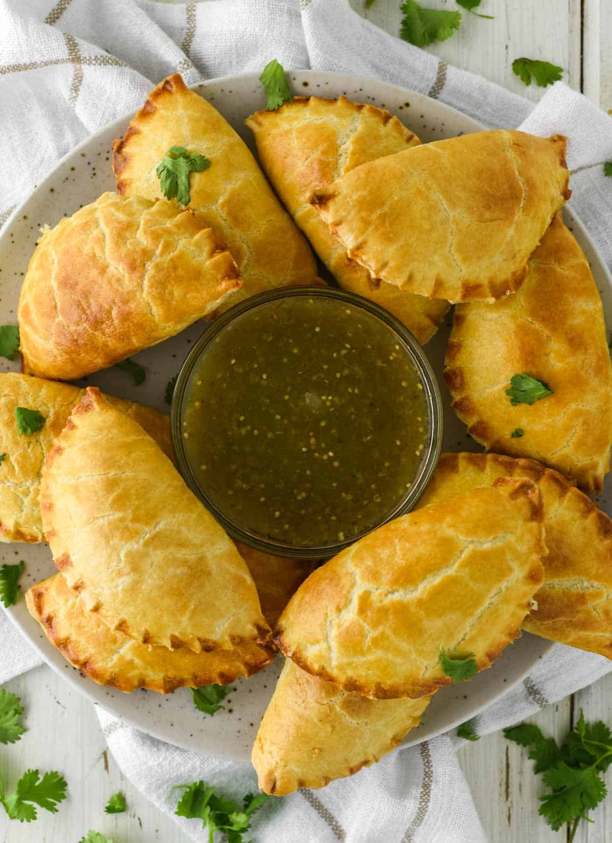 overhead shot of cheese empanadas on plate with bowl of salsa verde