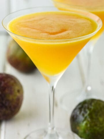 two glasses of passion fruit martinis with passion fruit on the board