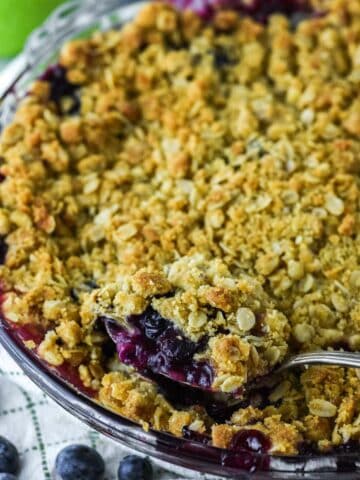 close-up of spoon lifting apple and blueberry crumble out of glass pie dish