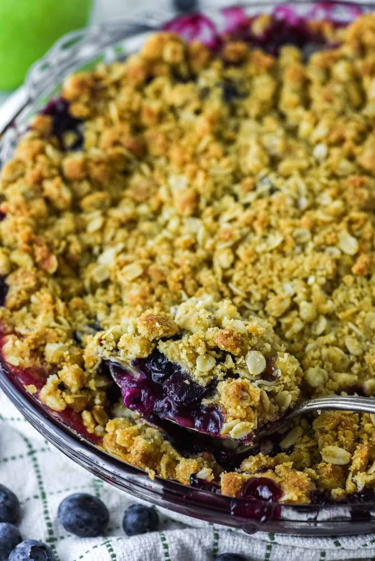close-up of spoon lifting apple and blueberry crumble out of glass pie dish