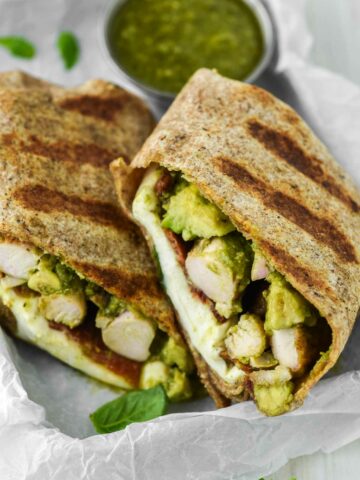 chicken pesto wrap stacked on parchment-lined sheet with bowl of pesto behind it