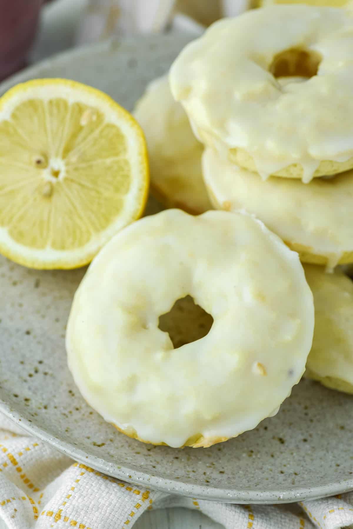close-up of lemon donuts stacked on speckled plate with lemon in background