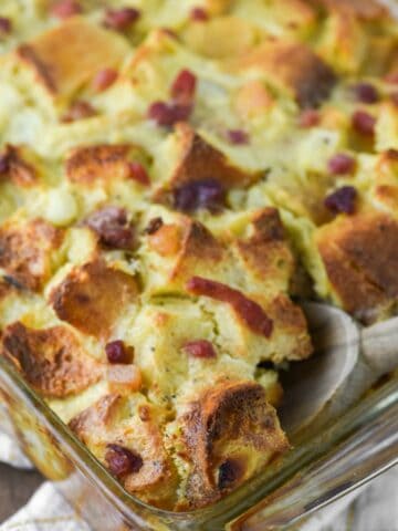 close-up of wooden spoon dipped in baking dish with cheese strata