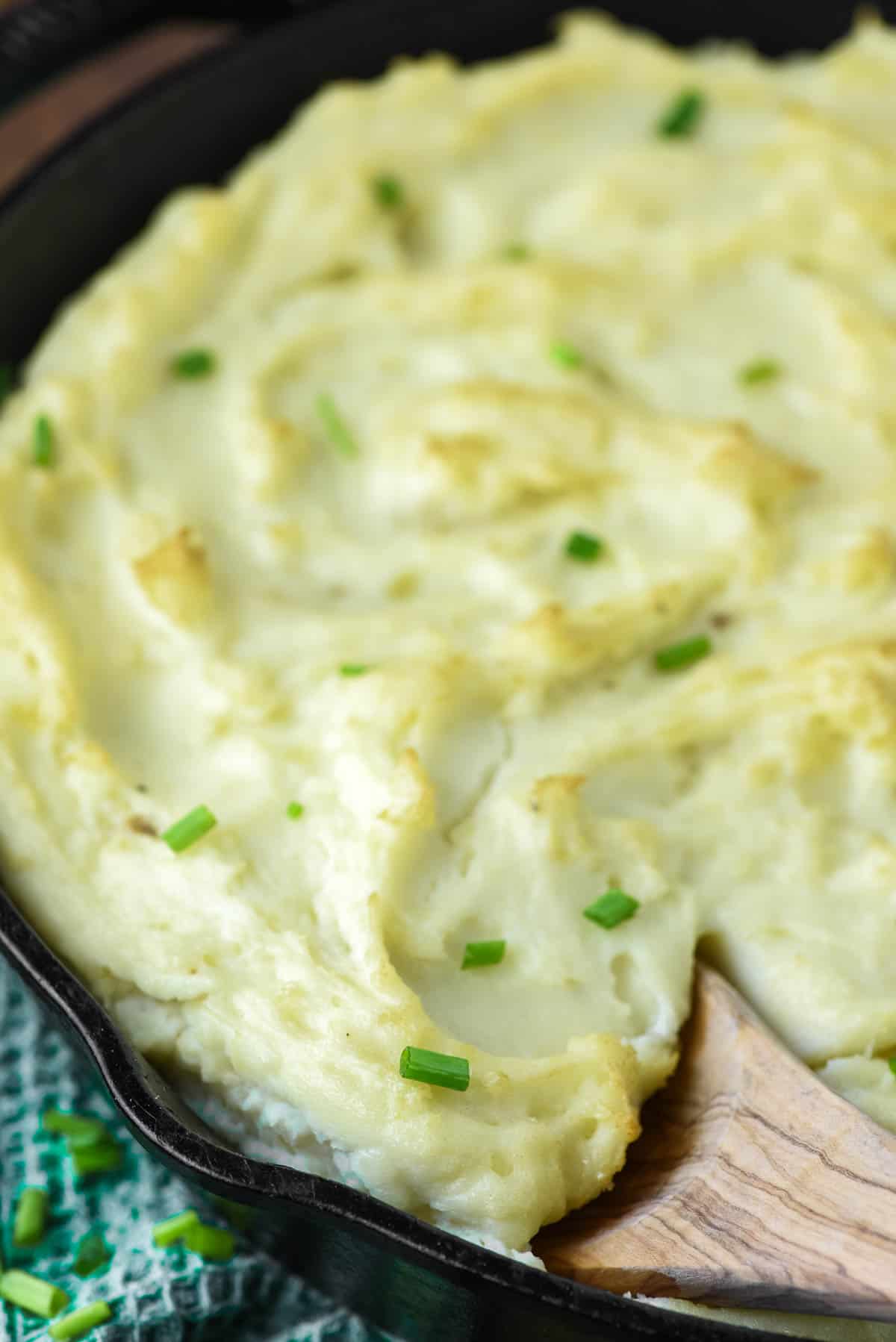 wooden spoon dipped in cast iron skillet with smoked mashed potatoes